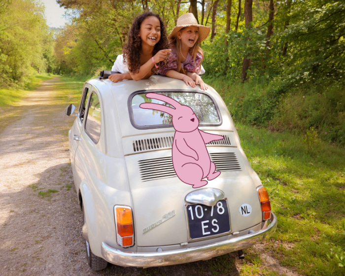 leren door te spelen Twee jonge meiden zitten in een auto met open dak en lachen vrolijk. Op de afbeelding is Happy de Haas, het haasje van Happy Kids Boutique, zichtbaar.