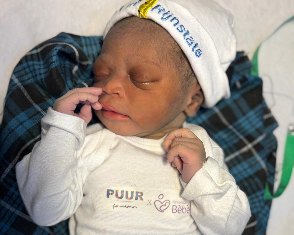 Pasgeboren baby met een mutsje van PUUR Foundation tijdens een geboortezorgproject in Gambia.